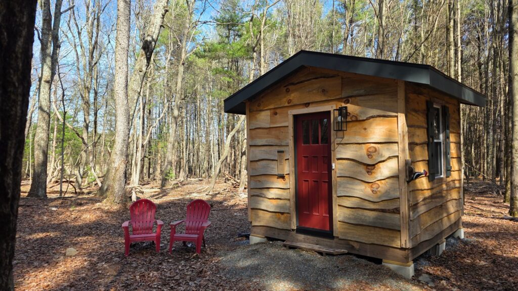 Wooden cabin with red chairs in forest.